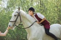 Brunette woman riding dark horse at summer green forest. Royalty Free Stock Photo