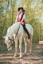 Brunette woman riding dark horse at summer green forest. Royalty Free Stock Photo