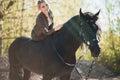 Brunette woman riding dark horse at summer green forest. Royalty Free Stock Photo
