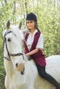 Brunette woman riding dark horse at summer green forest. Royalty Free Stock Photo