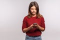 Brunette woman in shaggy sweater using mobile phone with attentive serious expression, typing or reading message on social network