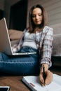 Brunette woman sitting on the floor with laptop and take note left hand.