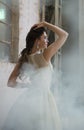 Brunette woman standing amidst fog next to rustic industrial buildings