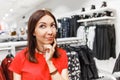 Brunette woman, thinking about shopping clothes in the fashion clothes store. Making right choice concept