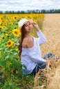 Brunette woman in white blouse sitting on a background of golden wheat and sunflowers fields Royalty Free Stock Photo