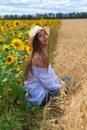 Brunette woman in white blouse sitting on a background of golden wheat and sunflowers fields Royalty Free Stock Photo