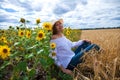 Brunette woman in white blouse sitting on a background of golden wheat and sunflowers fields Royalty Free Stock Photo