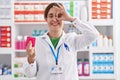 Brunette woman working at pharmacy drugstore holding condom smiling happy doing ok sign with hand on eye looking through fingers