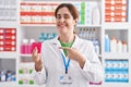 Brunette woman working at pharmacy drugstore holding condom smiling happy pointing with hand and finger