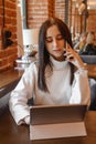 A brunette woman is working on a tablet at a table in a cafe. The theme of freelancing and free work schedule