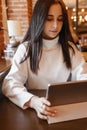 A brunette woman is working on a tablet at a table in a cafe. The theme of freelancing and free work schedule