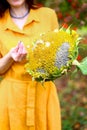 Brunette woman in yellow dress holds in hands ripe homemade sunflower with seeds. Autumn harvest photoshoot in garden. Helianthus