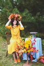 Brunette woman in yellow dress, maple leaves wreath on wooden chair by round table with blue tablecloth. Autumn harvest, nature Royalty Free Stock Photo