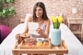 Brunette young woman eating breakfast in the bed reading a letter smiling looking to the side and staring away thinking Royalty Free Stock Photo