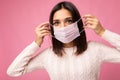 Brunette young woman holds and wears a white medical mask to protect yourself from corona virus, cares for her health