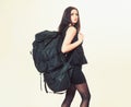 Brunette young woman in short black dress walking with huge heavy rucksack isolated on white background. Conceptual