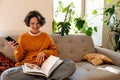 Brunette young woman using cellphone and reading book on couch Royalty Free Stock Photo