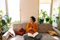 Brunette young woman using cellphone and reading book on couch Royalty Free Stock Photo