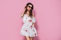 Brunnet girl in floral summer dress and sunglasses posing on a pink background. Summer floral outfit Royalty Free Stock Photo