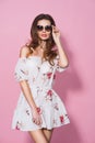 Brunnet girl in floral summer dress and sunglasses posing on pink background. Stylish wavy hairstyle Royalty Free Stock Photo