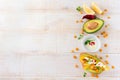 Bruschetta with avocado, yellow pepper, grains of corn, parsley and chili pepper on a light wooden background.