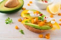 Bruschetta with avocado, yellow pepper, grains of corn, parsley and chili pepper on a light wooden background.