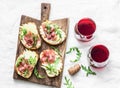 Bruschetta with cream cheese, pear, prosciutto, arugula on wooden chopping board and red wine on light background, top view