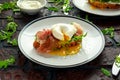 Bruschetta with cream cheese, wilde rucola, parma ham and poached egg served on white plate. Royalty Free Stock Photo