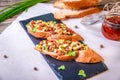 Bruschetta with feta cheese, dried tomatoes, olive oil and fresh microgreen herbs, on a stone plate on a wooden table.