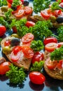 Bruschetta with green and black olives, feta cheese, cherry tomatoes, parsley and red pepper on black background Royalty Free Stock Photo