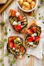 Bruschetta with grilled eggplant, cherry tomatoes, feta cheese, capers and fresh aromatic herbs on a wooden table. Delicious Medit