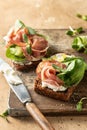 Bruschetta with prosciutto, cream cheese, cucumber, spinach and microgreens. Tasty sandwich or toasted bread on wooden Royalty Free Stock Photo