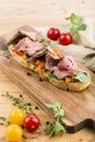 Bruschetta with roast beef, fresh herbs and paprika on a board on a light wooden background