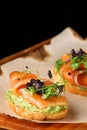 Bruschetta with salmon closeup. tapas with salmon on guacamole and topped microgreen on wooden board and black background