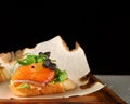 Bruschetta with salmon closeup. tapas with salmon on guacamole and topped microgreen on wooden board and black background