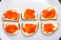 Bruschettes with butter and red caviar on a white plate laid out along a gray concrete background