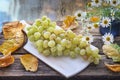 A brush of grapes in a wooden cup, old wooden table white cutting board Royalty Free Stock Photo