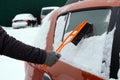 Brush in mans hand. Man in gray gloves clears orange car from snow. Remove lot of snow from auto