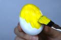 Brush painting an Easter egg with yellow paint. Selective focus. Close-up