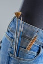 Brushes and pencils in the pocket of the girl`s jeans on a gray background. Artist painting concept