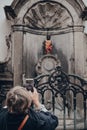 Woman takes photo of Manneken pis landmark bronze fountain sculpture in Brussels, Belgium