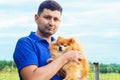 Brutal attractive man smiling and holding pomeranian spitz in hands. owner hugging the dog