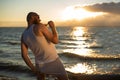 A brutal bald man posing on the beach at sunset in his underwear and touching his red beard. A parody of a glamorous Royalty Free Stock Photo