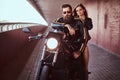 Brutal bearded biker in a black leather jacket with sunglasses and sensual brunette girl sitting together on a custom Royalty Free Stock Photo