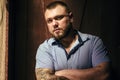 Brutal bearded man with a tattoo on his arm, a portrait of a man in dramatic light against a brown wooden wall, attractive bearded