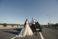 Brutal couple, the bride and groom, with a bat in leather jackets near the car on the road