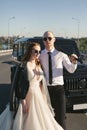 Brutal couple, the bride and groom, with a bat in leather jackets near the car on the road