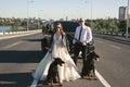 Bride and groom, in black glasses and leather jackets with Dobermans near the car on the road