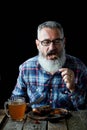 Brutal gray-haired adult man with a beard eats mustard steak and drinks beer, concept of a holiday, festival, Oktoberfest