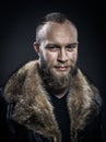 Brutal handsome smiling unshaven man with long beard and moustache in black fur coat with collar.